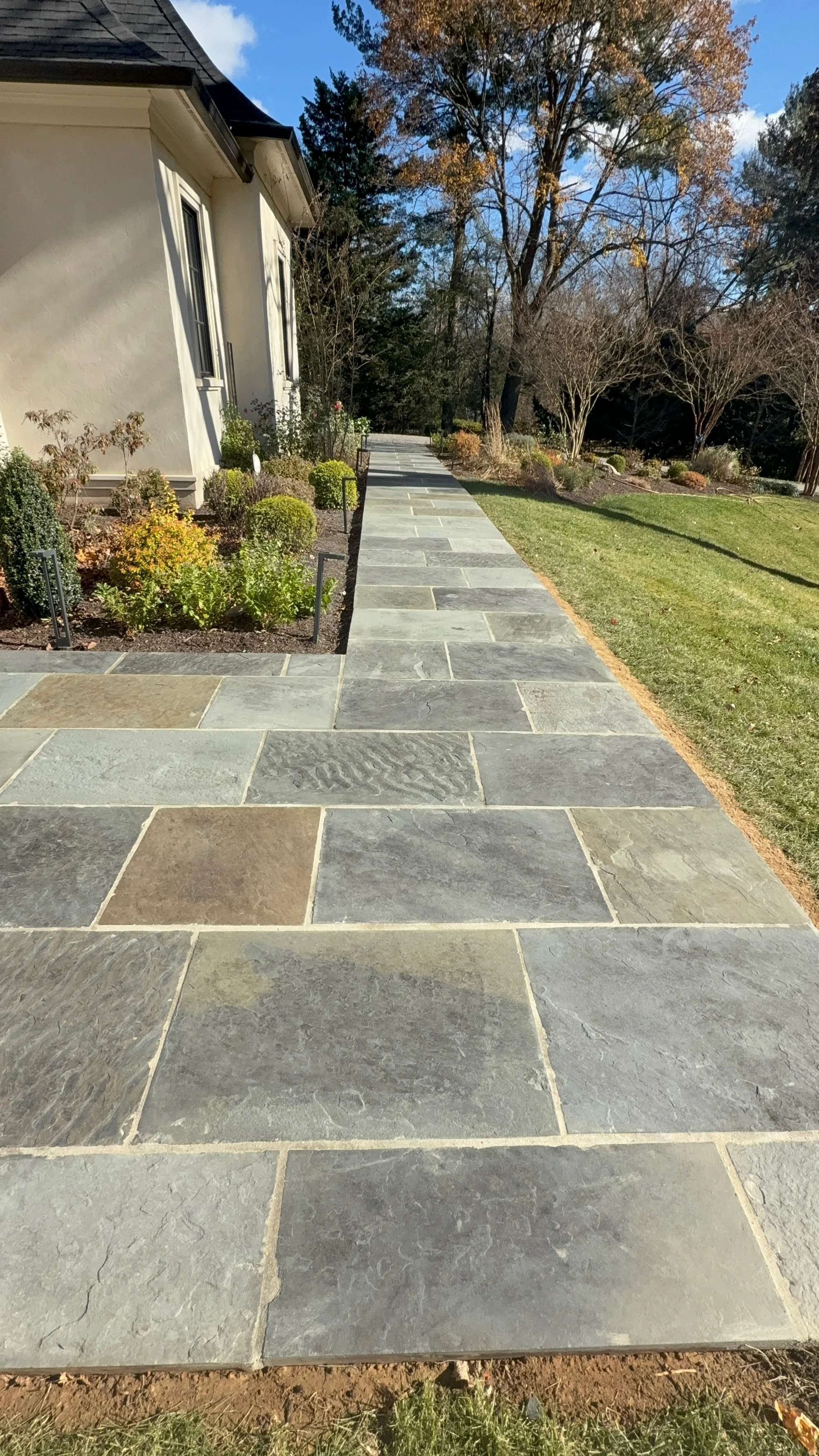 Gray and tan slate walkway with mortared joints leading from home entrance through landscaped yard