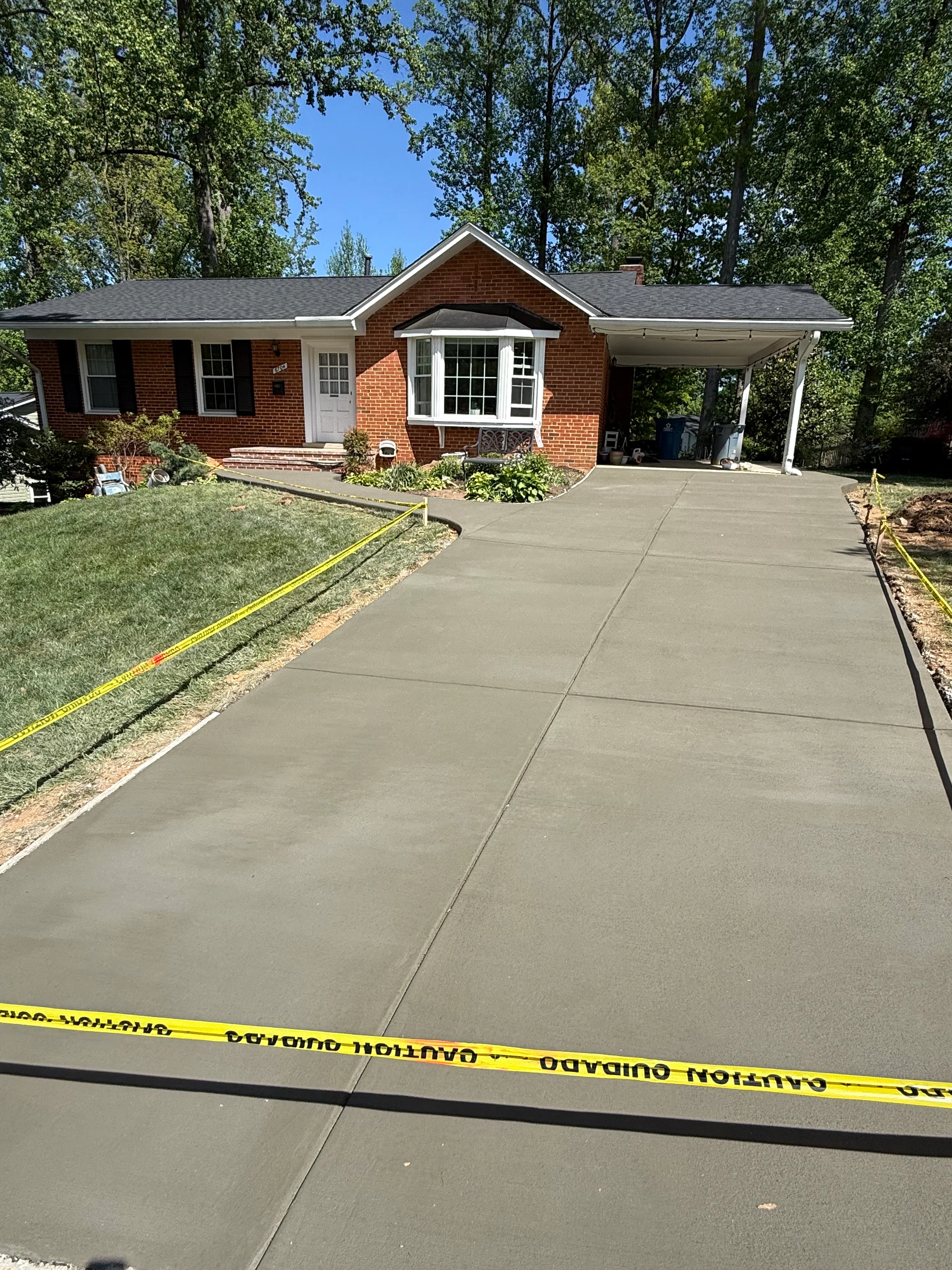 Newly poured concrete driveway with control joints leading to brick home with carport