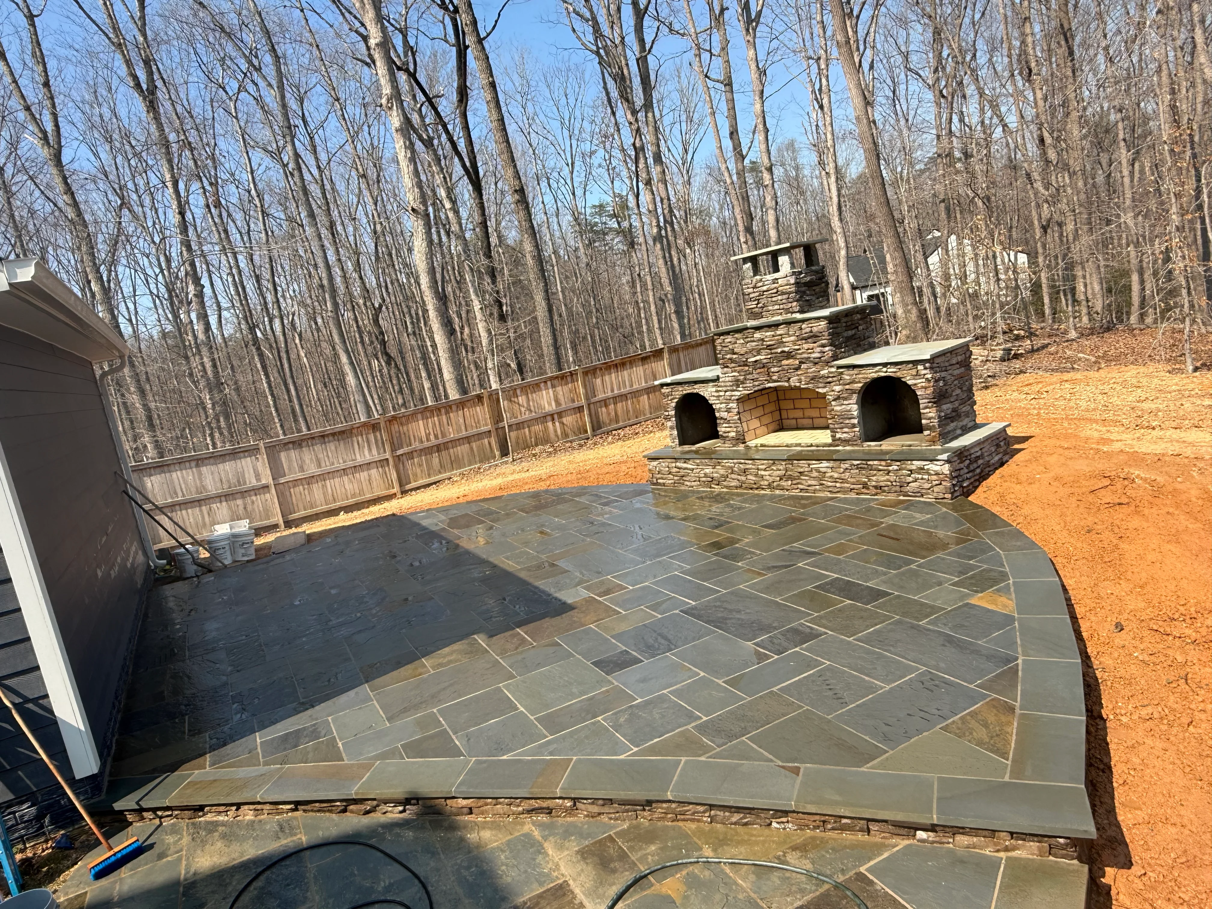 Stone patio with herringbone pattern and tiered stone fireplace in wooded backyard