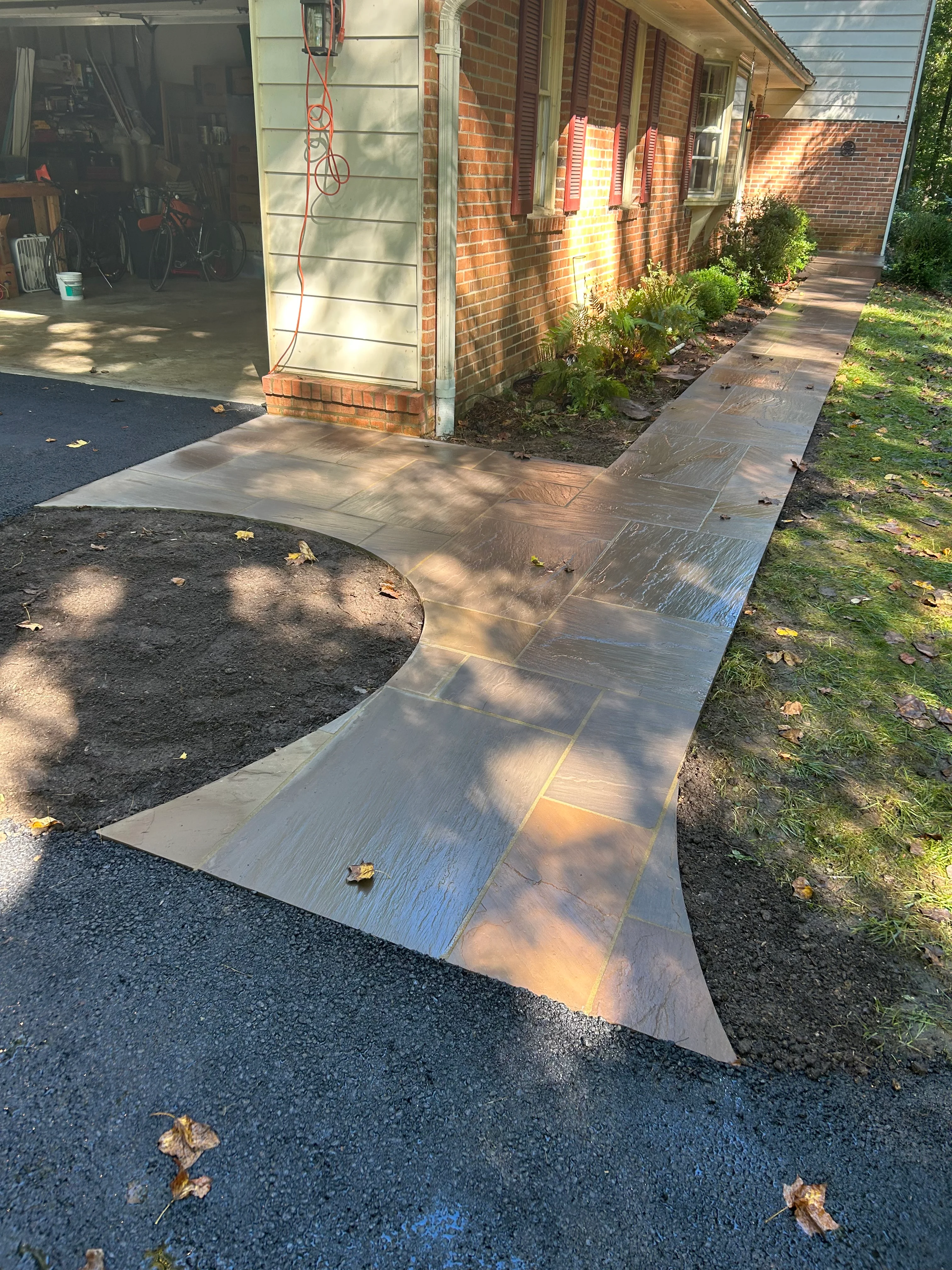 Curved flagstone walkway with wood-grain texture running along brick home exterior