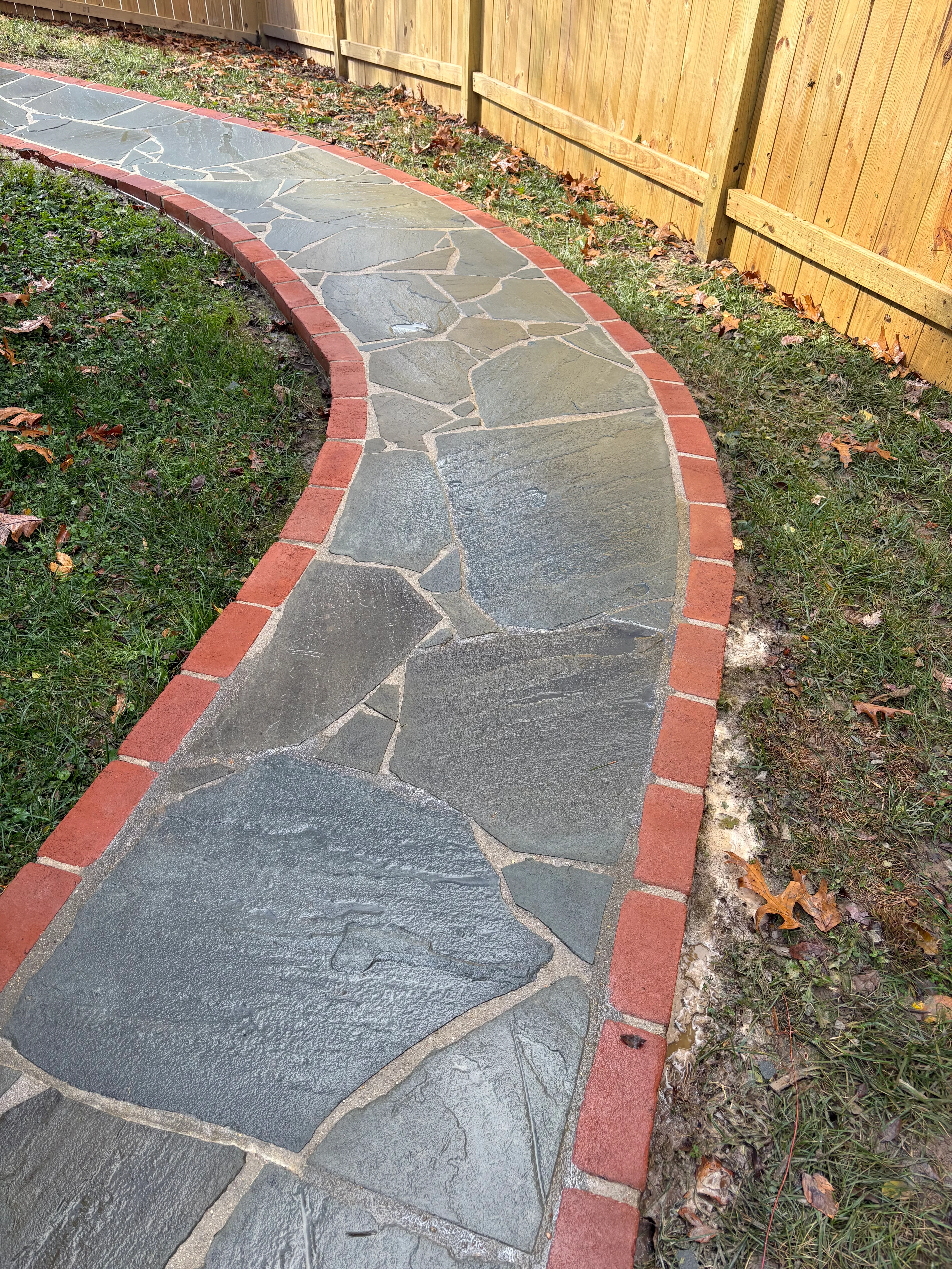 Curved flagstone pathway with red brick border in backyard
