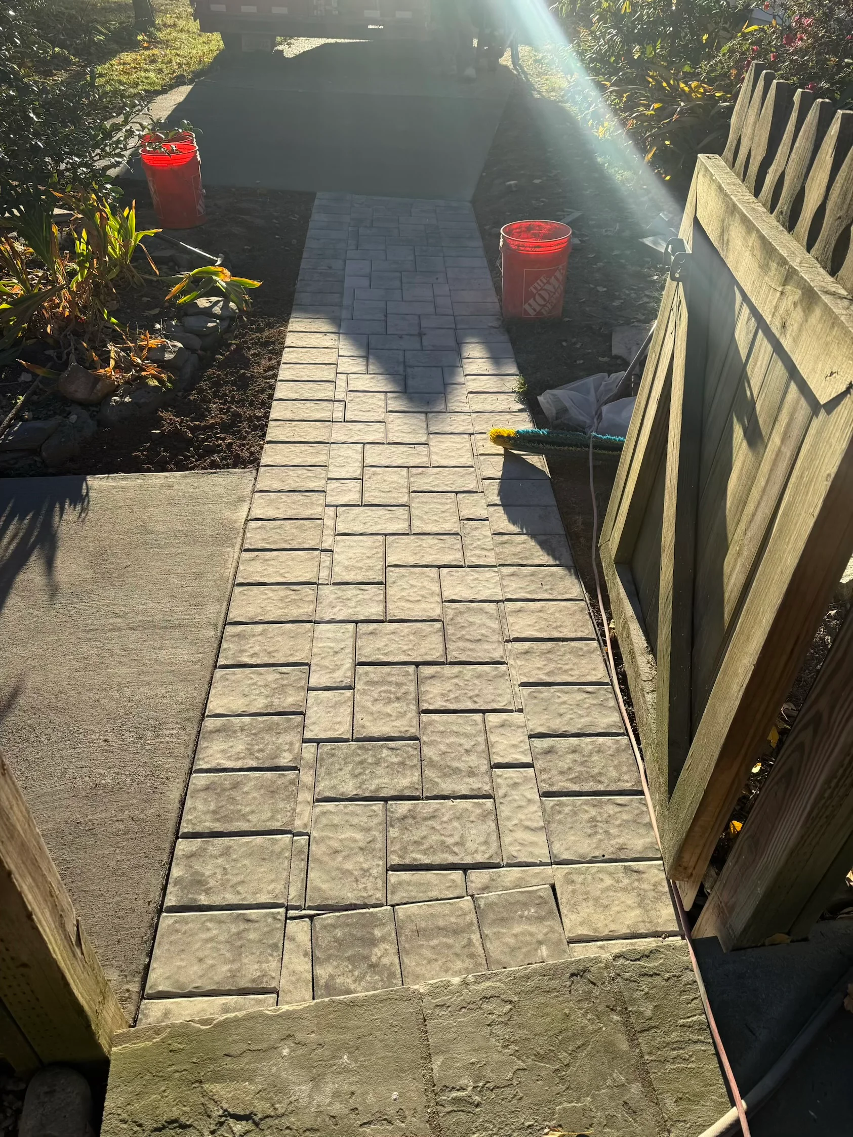 Stone paver walkway with running bond pattern between wooden fences and landscaping