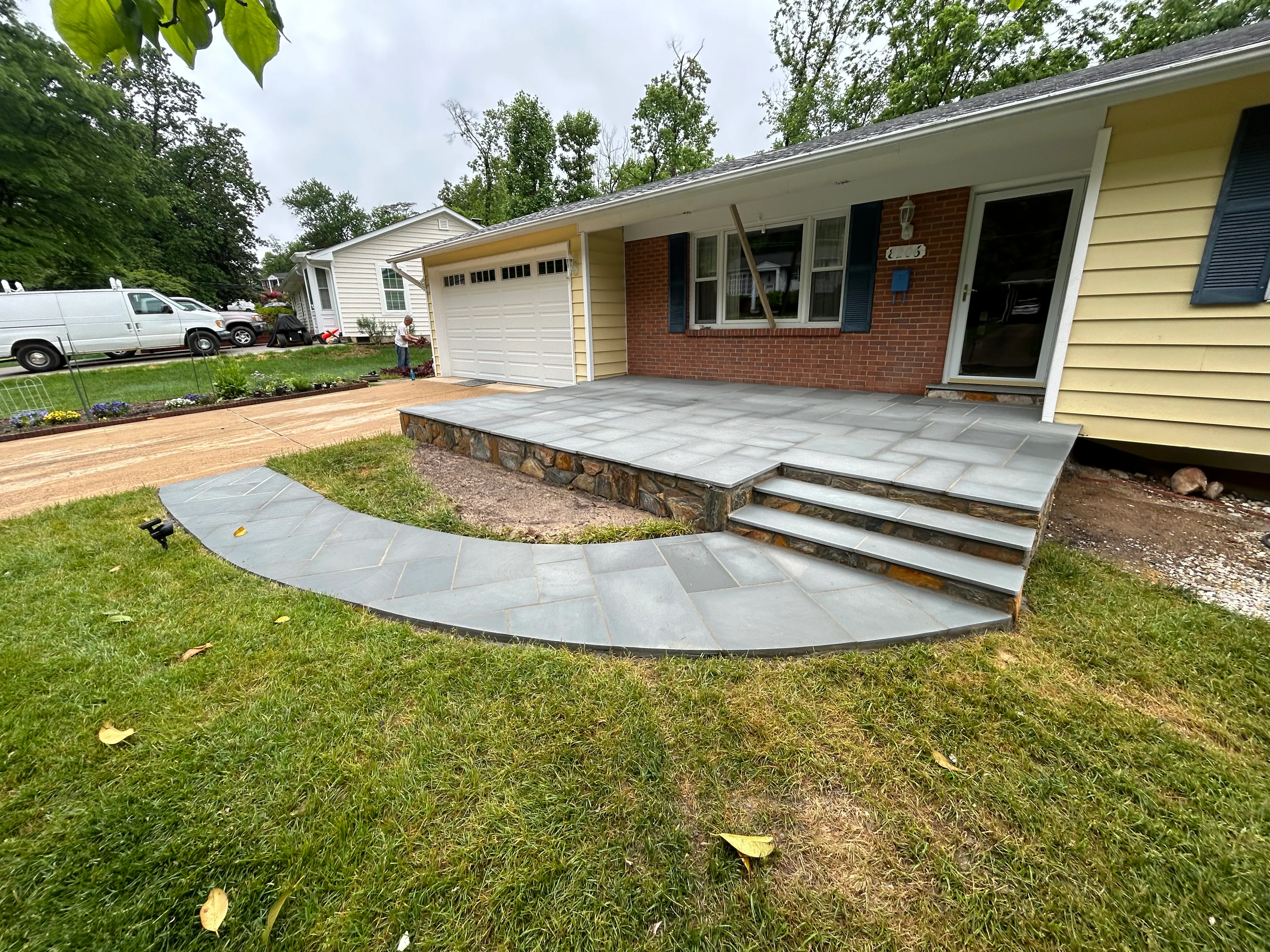Slate patio with curved walkway and stone steps in front of brick home