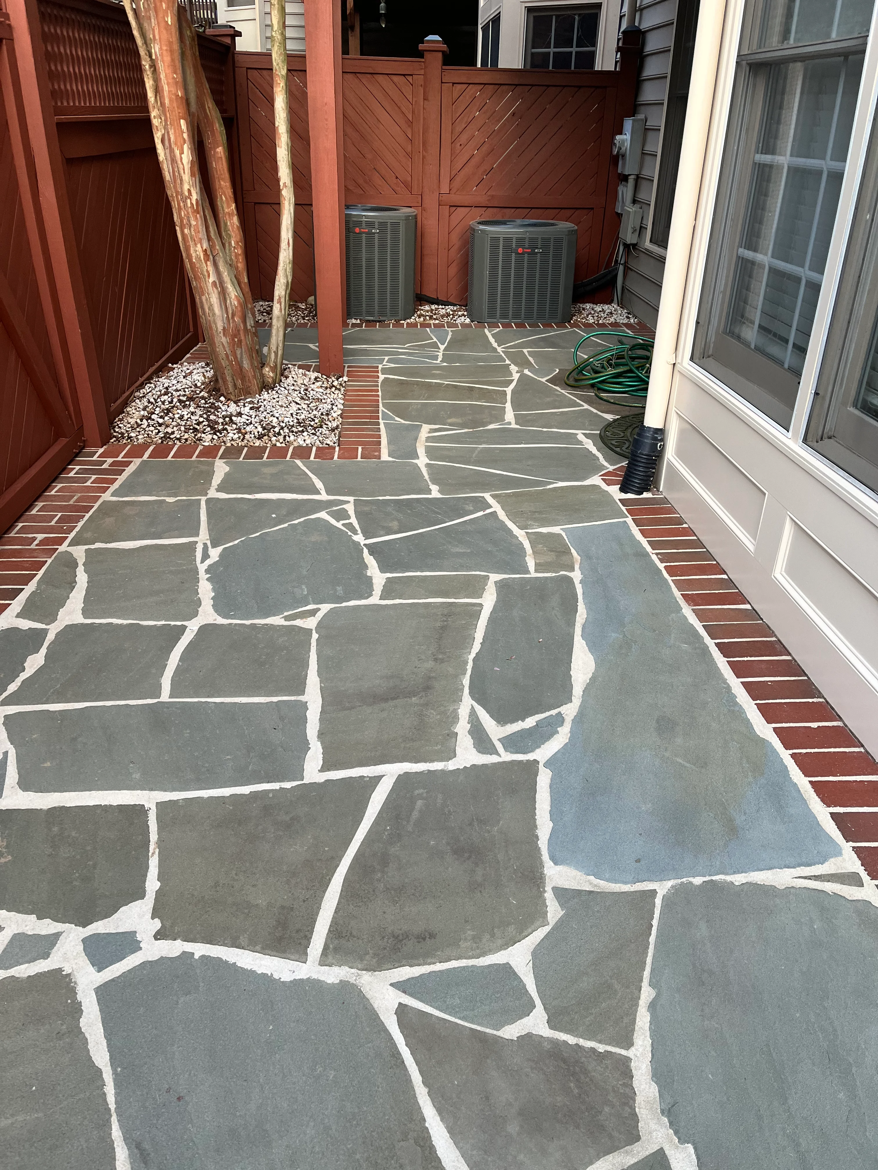 Gray flagstone patio with white mortar joints and red brick border in residential backyard