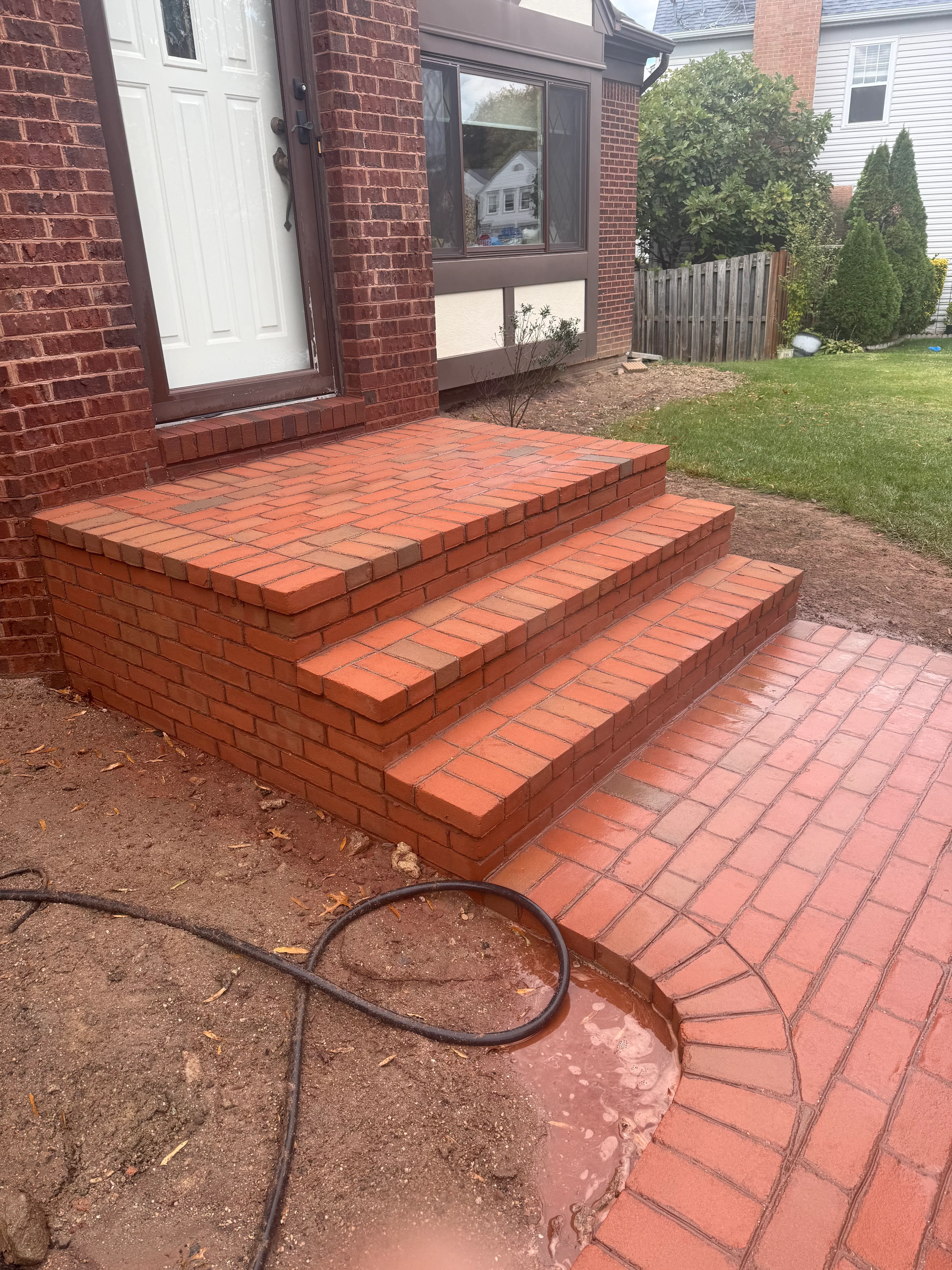 Newly installed brick patio steps with three tiers leading to backyard landing