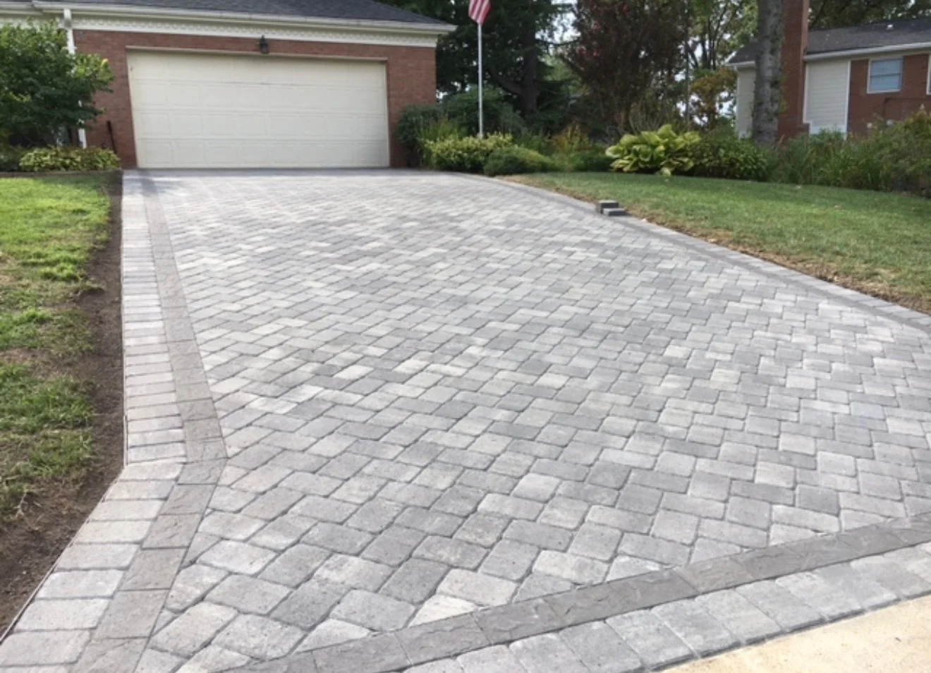 New gray permeable paver driveway with herringbone pattern and border edging in front of brick home