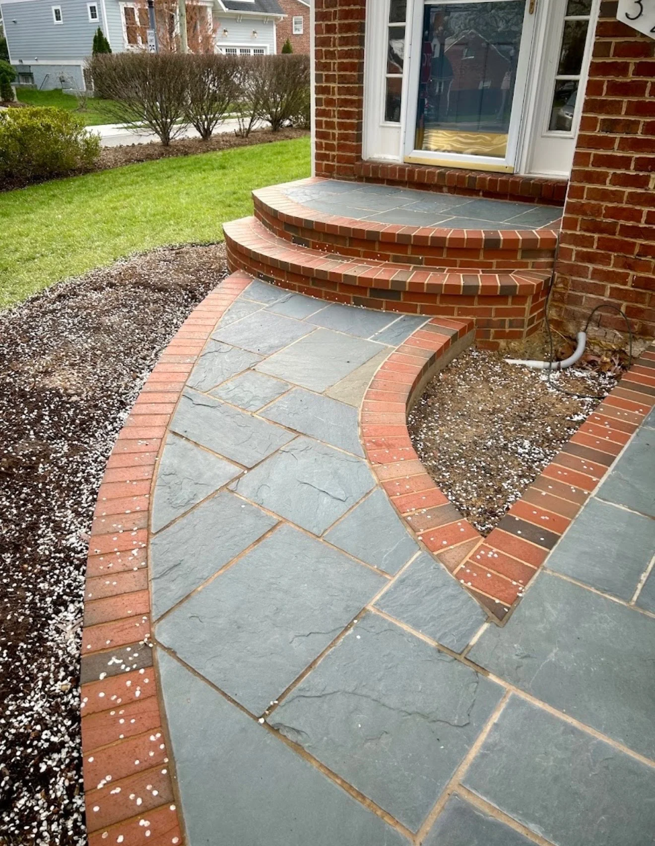 Curved slate patio with brick edging and steps leading to brick home entrance