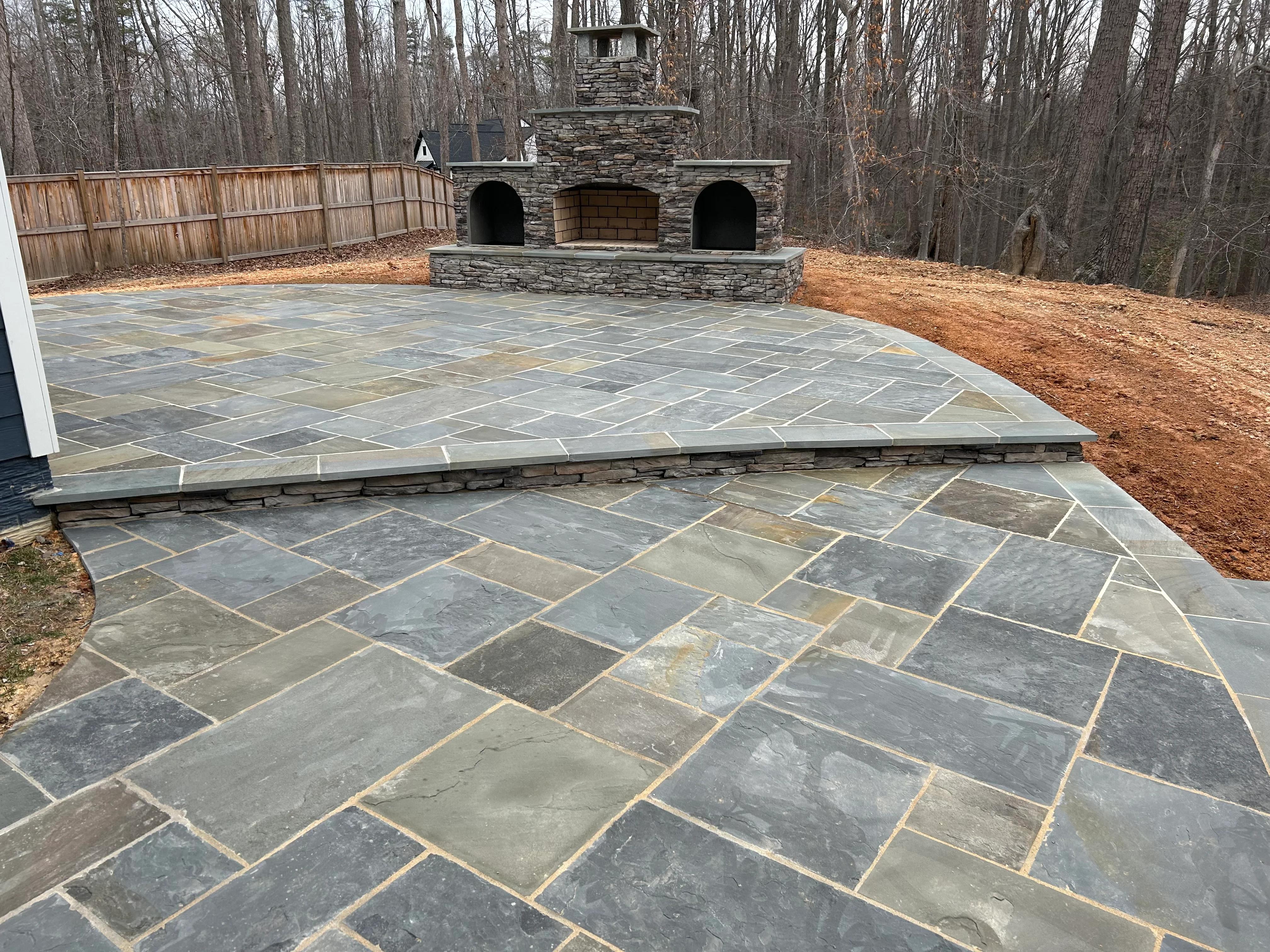 Flagstone patio with herringbone pattern and stacked stone fireplace with three arches
