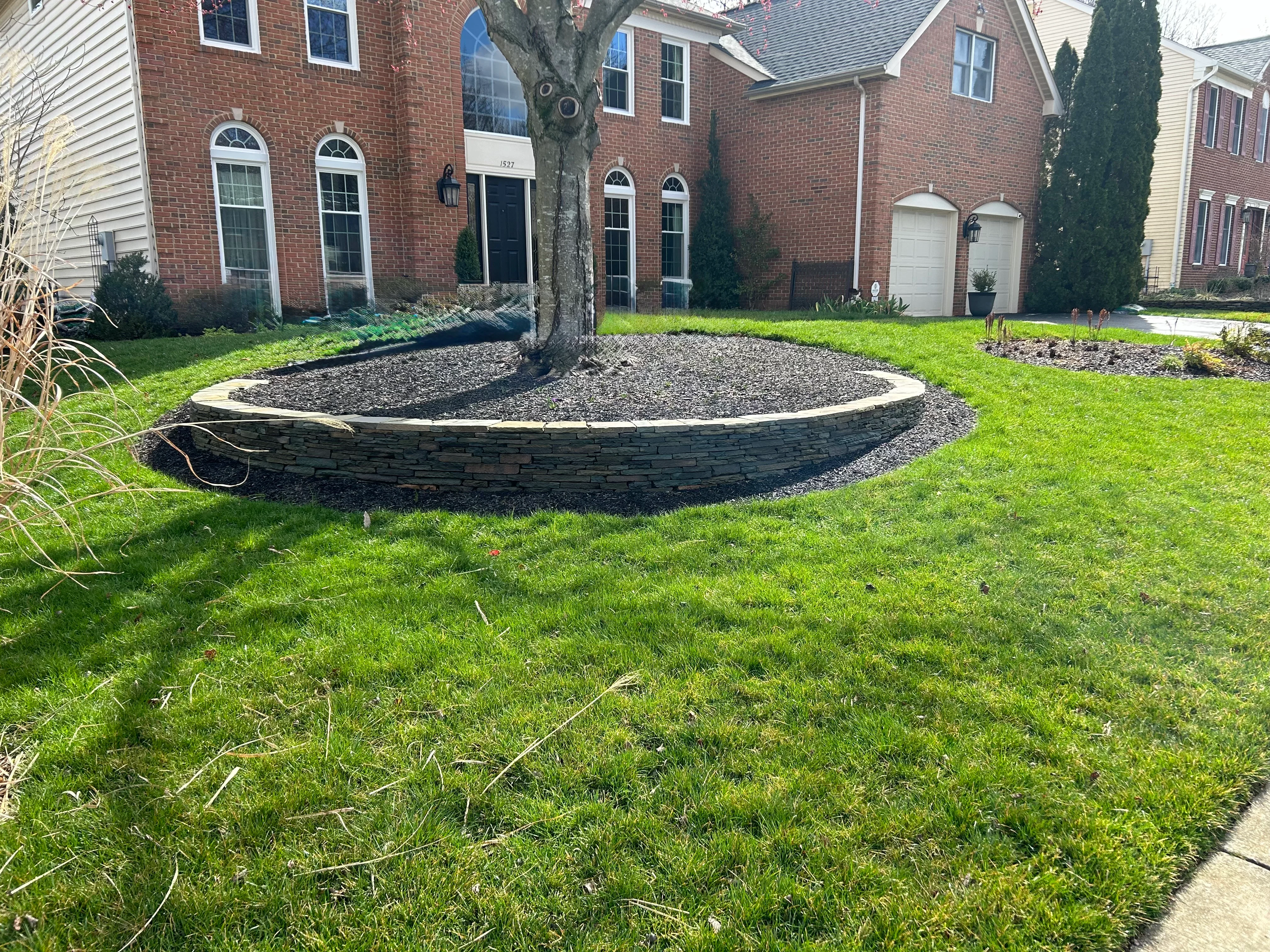 Curved stone retaining wall with gravel bed around tree in front yard