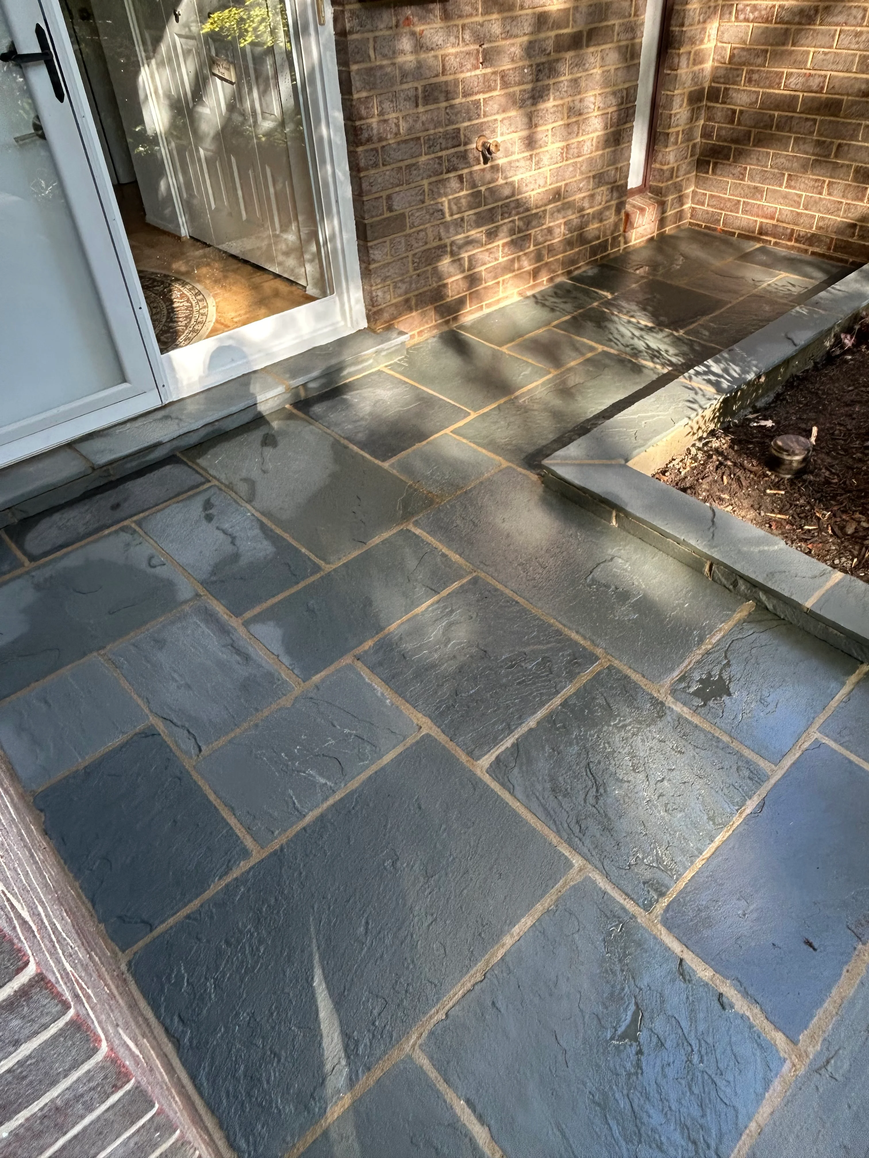 Dark slate patio with running bond pattern and tan mortar joints adjacent to brick home