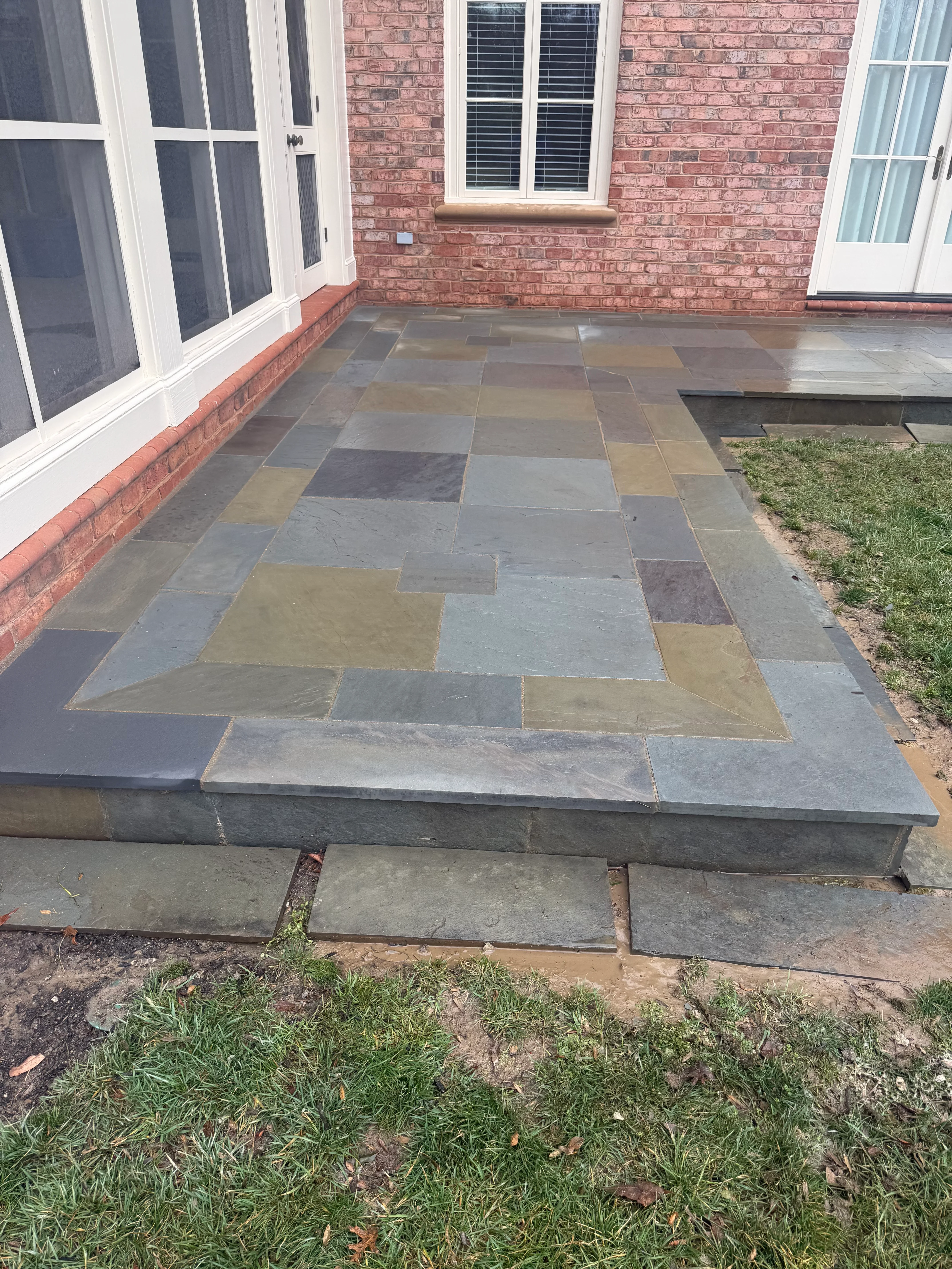 Mixed slate patio with geometric pattern in earth tones against brick home
