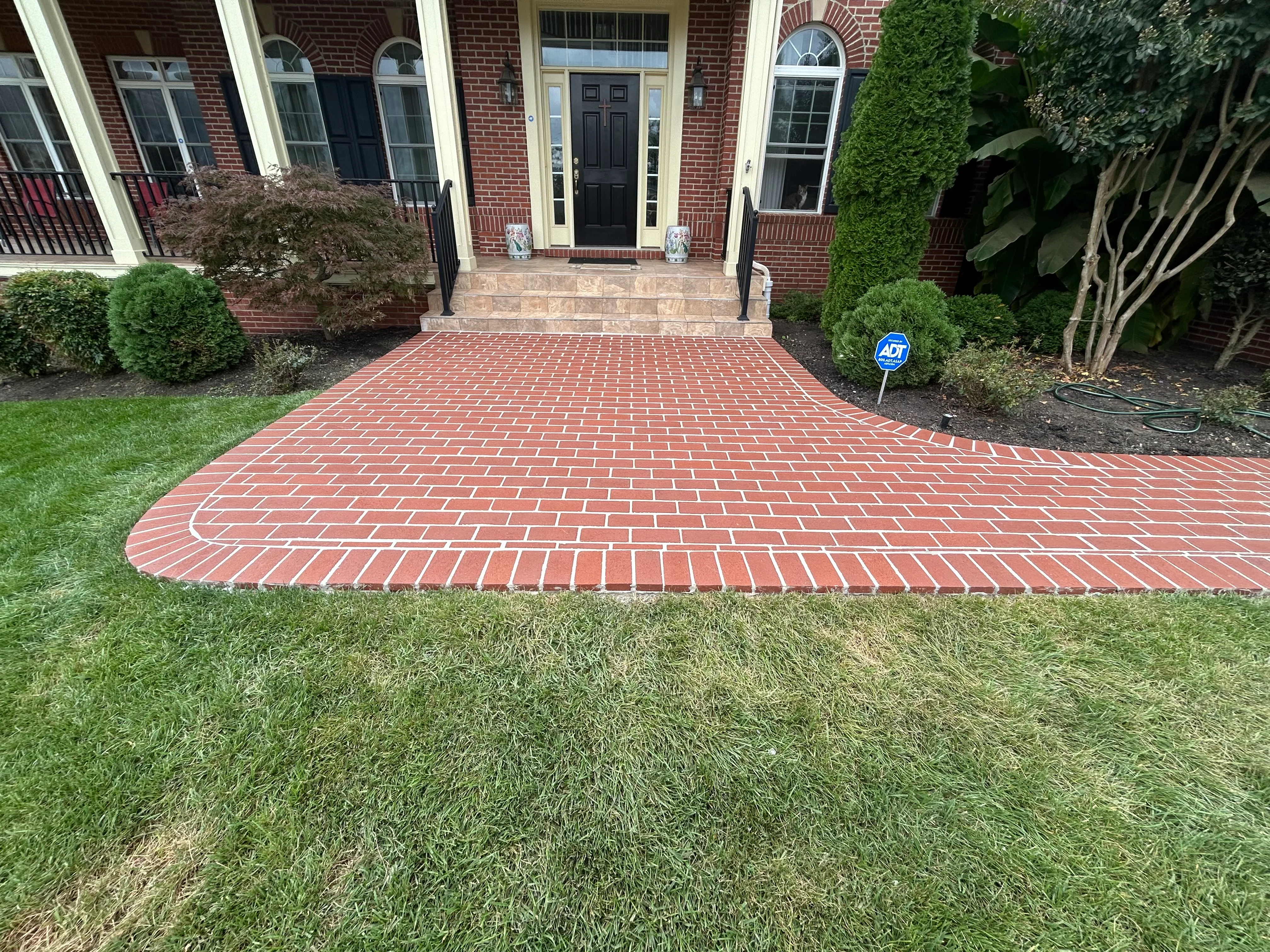 Red brick driveway with running bond pattern leading to brick colonial home entrance