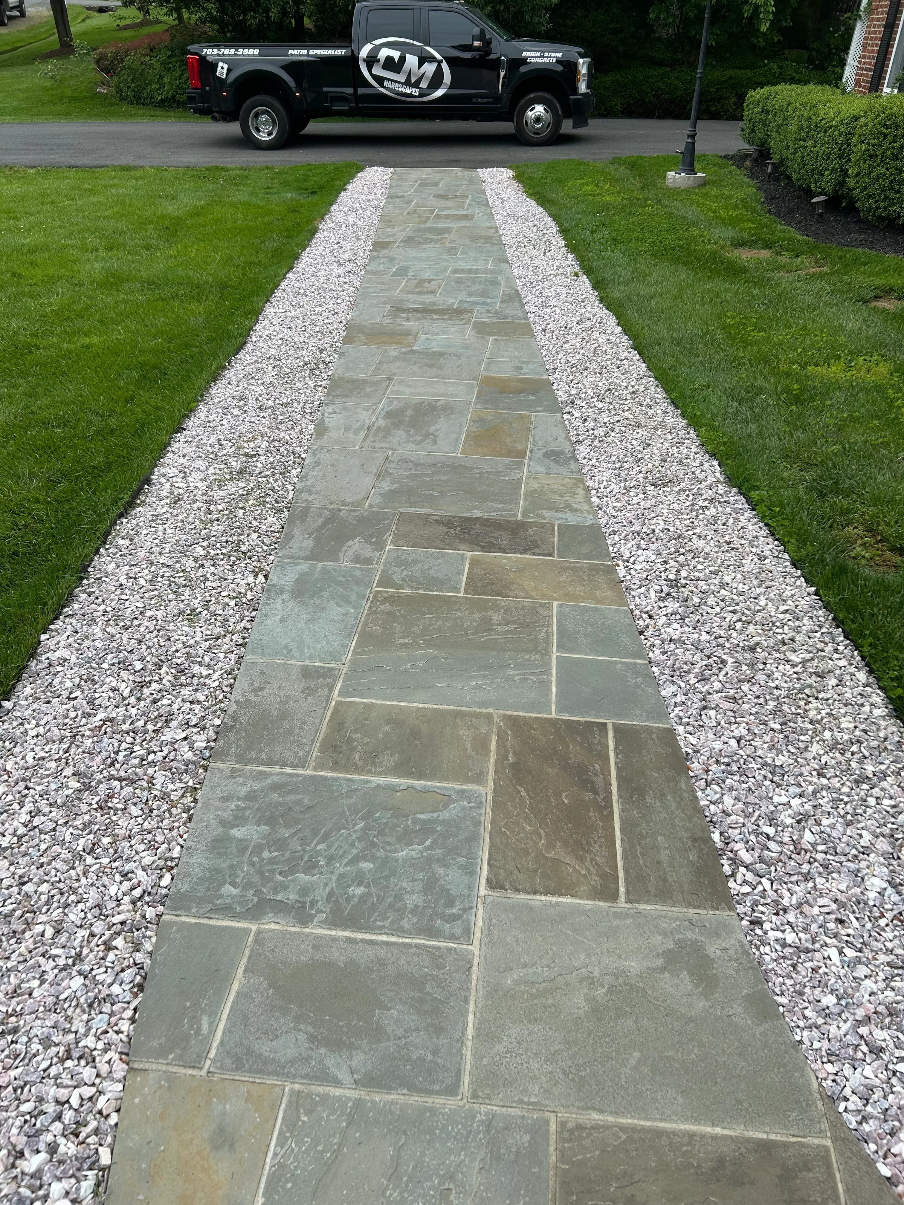 Slate stone walkway with white gravel borders leading through manicured lawn