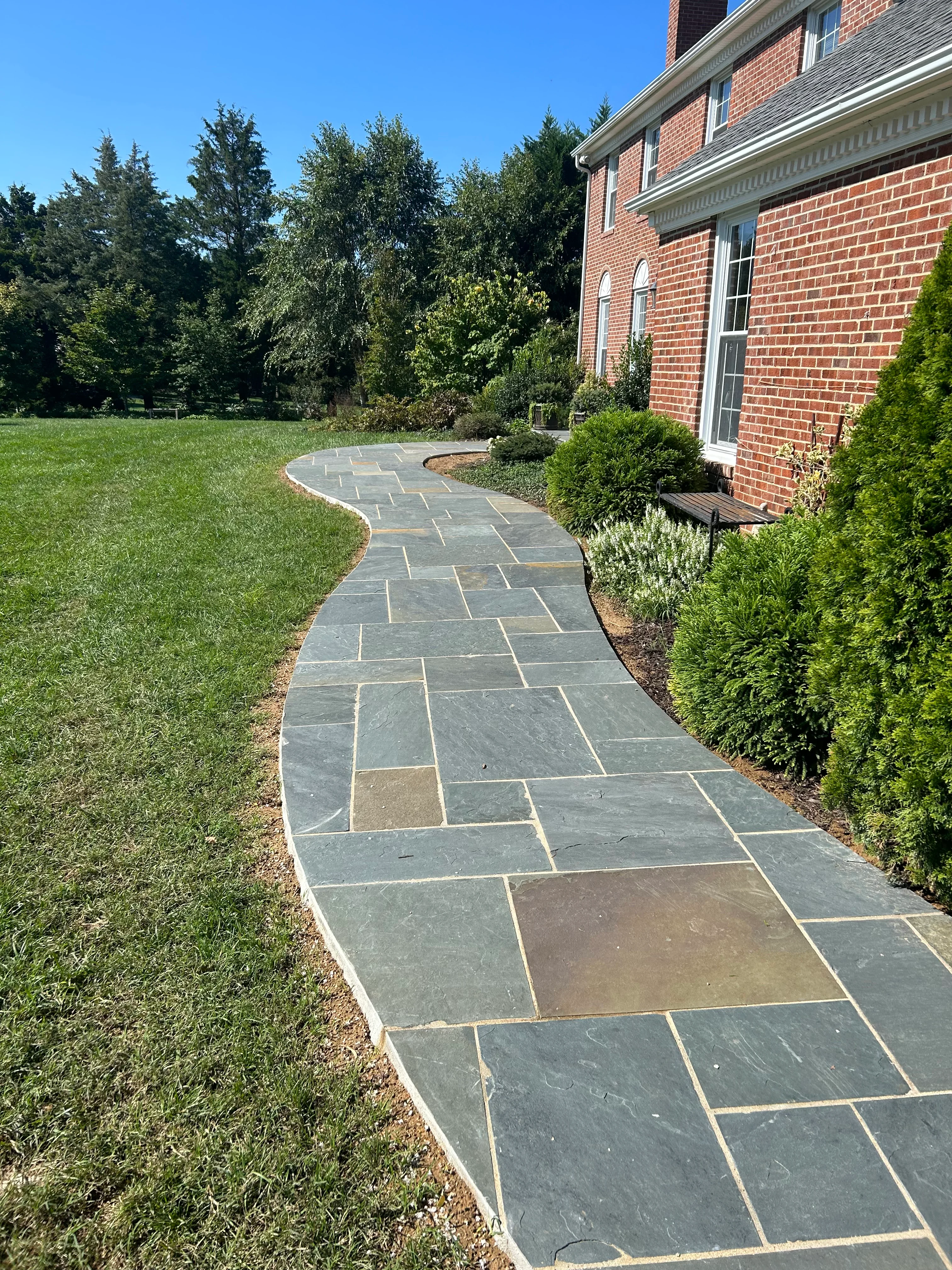 Curved slate walkway with charcoal and tan flagstones alongside brick home