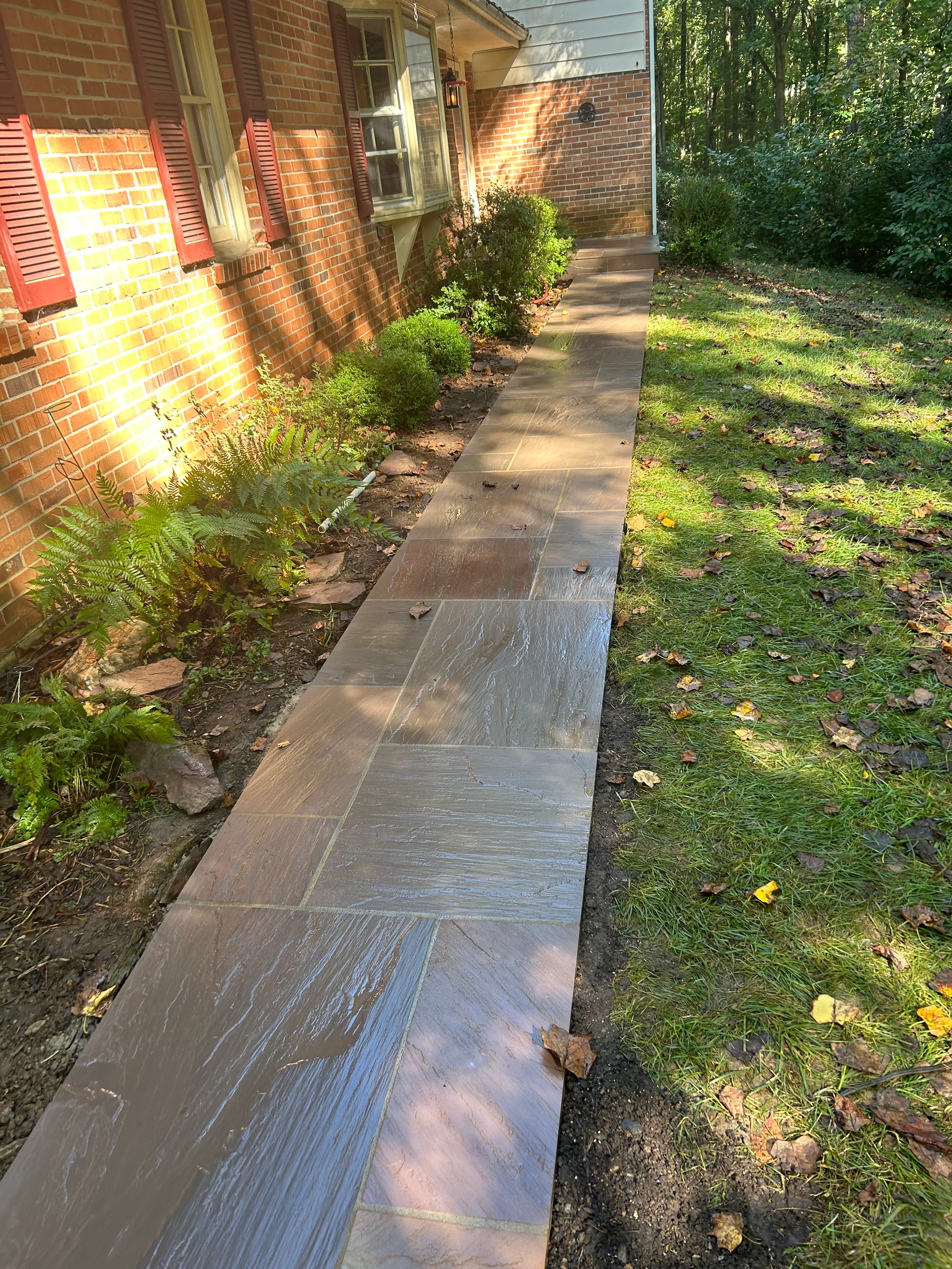 Slate tile walkway alongside brick home with landscaping and plantings